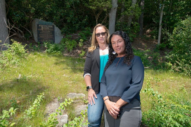 Herring Pond Wampanoag Tribe members Jamie Hoctor, left, and Kerina Silva stand on Tuesday near a stone that commemorates a tribal burying ground and meeting house on a thickly wooded hillside off Scenic Highway in Bourne.  Tribe members plan to ask for $7,000 in Community Preservation Act money at the fall town meeting to conduct ground-penetrating radar to learn more about who or what is buried on the hillside.